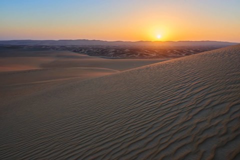 Atmospheric picture of a desert at sunset with undulating sand dunes, calm and peaceful atmosphere,
