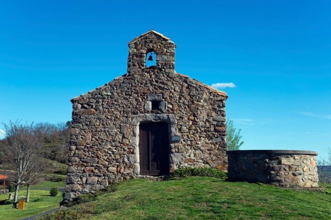 Historische Kirche aus Stein mit kleinem Glockenturm, umgeben von Gras und einem klaren blauen