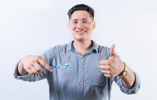 Smiling young man holding a toothbrush gesturing OK. Person holding toothbrush with thumbs up. Guy