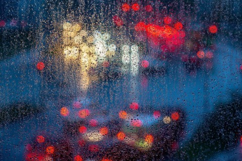 Rainy weather, road traffic, raindrops on a window pane, behind, blurred, lights of vehicles on a