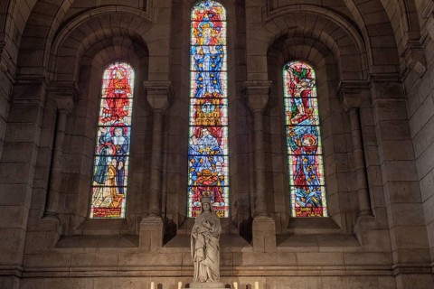 Stained glass windows illuminate a statue in a church, warm light floods in, Paris