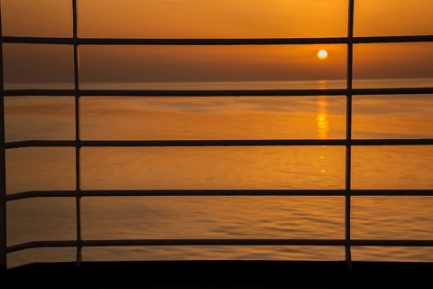 Close-up of silhouetted railing on cruise ship and golden setting sun over Adriatic sea near Zadar,