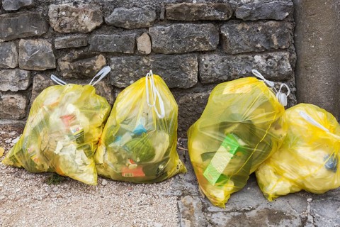 Close-up of translucent yellow plastic thrash bags filled with various discarded domestic garbage,