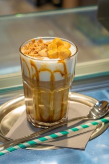 A glass of iced coffee with cream and caramel on a tray, served with a straw and spoon, autumn
