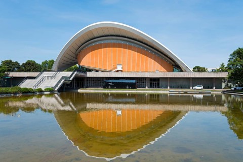 Modern building with curved roof, reflected in the water against a clear sky, House of World