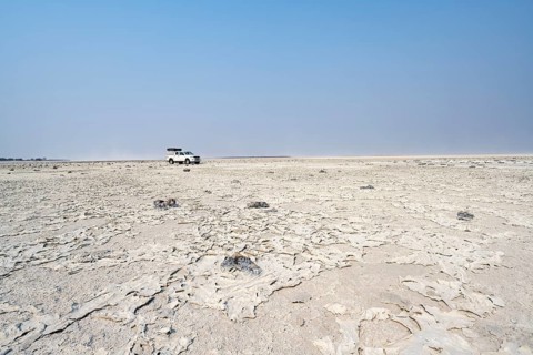 Four-wheel drive Toyota Hilux with roof tent, driving over salt pan, lone car in large wide plain,