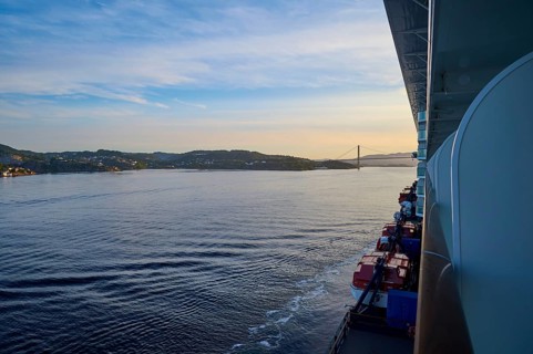 A cruise ship, Mein Schiff 6, on the calm sea, in the background a bridge and hills at sunset,