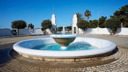 Round fountain with splashing water surrounded by architectural structures and palm trees, thermal