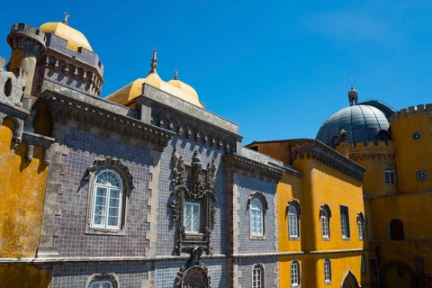 Part of a castle with yellow and grey facades, a dome and windows under a blue sky, Palácio
