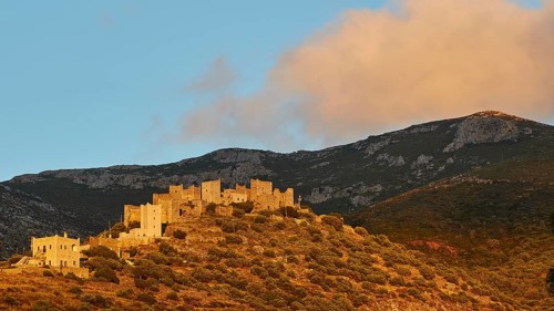 Sunset illuminates the historic buildings and the hilly landscape, Vathia, residential tower