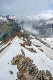Mountaineer on a rocky ridge with snow, descent from the summit of Schönbichler Horn, view of