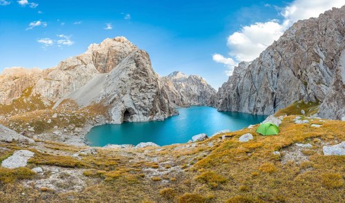 Green tent at the turquoise mountain lake Kol Suu with rocky steep mountains, Kol Suu Lake, Sary
