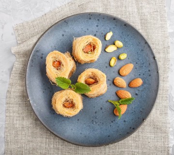 Kunafa, traditional arabic sweets in blue ceramic plate on a gray concrete background. top view,
