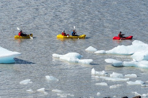 A group of tourists paddles in kayaks between icebergs, glacial lake Fjallsárlón, glacier