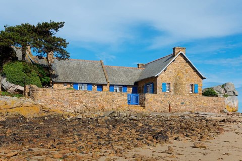 Stone house with blue shutters and a sandy forecourt on a rocky coast, house on the Plage de