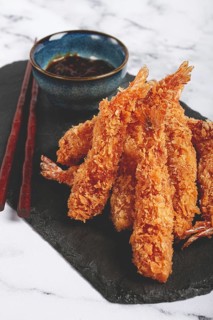 Shrimp in tempura, deep fried, on black slate, with sauce, light marble table, no people
