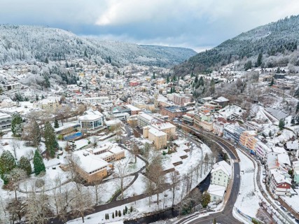 Bird's eye view of a snow-covered town with a river, surrounded by hills and green trees, Bad