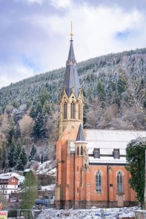Gothic church tower facade with snow-covered mountain forest in the background, Bad Wildbad, St
