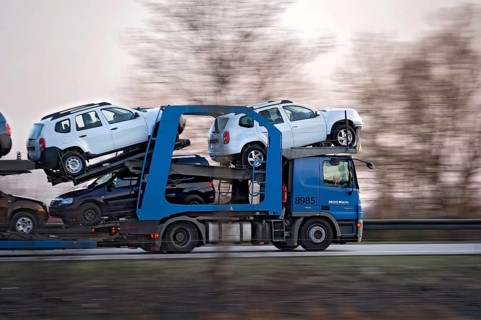 Truck, lorry, articulated lorry with new Dacia cars driving fast on the A92 motorway, motion blur,