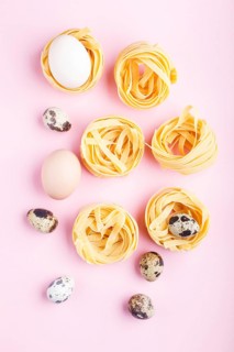 Raw uncooked tagliatelle pasta with quail eggs on a pink pastel background. top view, copy space