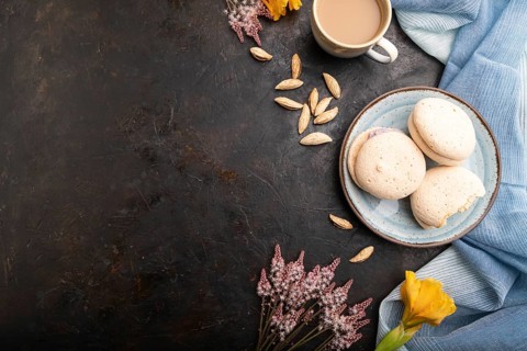 Meringues cakes with cup of coffee on a black concrete background and blue linen textile. Top view,