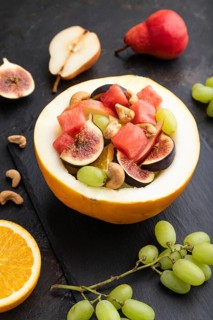 Vegetarian fruit salad of watermelon, grapes, figs, pear, orange, cashew on slate board on a black