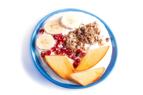 A blue plate with greek yogurt, granola, persimmon, banana, pomegranate isolated on white