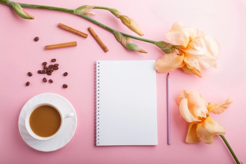 Orange iris flowers and a cup of coffee with notebook on pastel pink background. Morninig, spring,