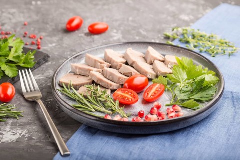 Boiled pork tongue with tomatoes and herbs on a black concrete background and blue linen textile.