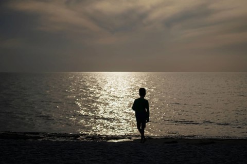 A child stands alone on the beach in the backlight of the setting sun. Born, 01.08.2024