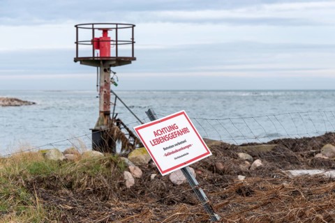 Beacon behind a fence with warning sign 'ACHTUNG LEBENSGEFAHR', cloudy sky over the sea, entrance