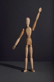 Wooden mannequin stands with raised hand on gray background. protest, attention concept. copy