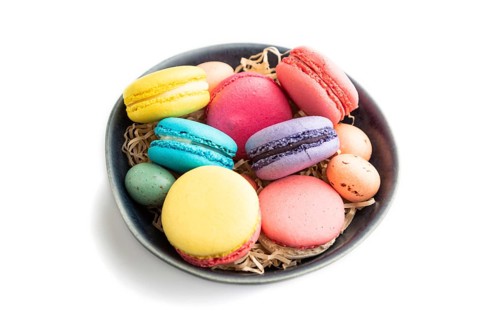 Multicolored macaroons and chocolate eggs in blue ceramic bowl isolated on white background. side