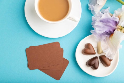 Brown business card with cup of cioffee, chocolate candies and iris flowers on blue pastel
