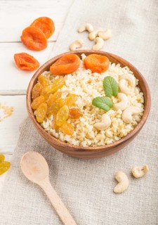 Bulgur porridge with dried apricots, raisins and cashew in wooden bowl on a white wooden background