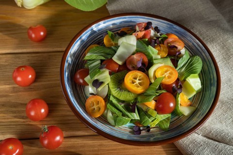 Vegetarian salad of pac choi cabbage, kiwi, tomatoes, kumquat, microgreen sprouts on a wooden