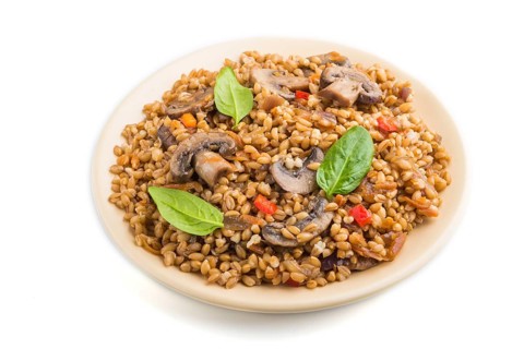 Spelt (dinkel wheat) porridge with vegetables and mushrooms on ceramic plate isolated on white
