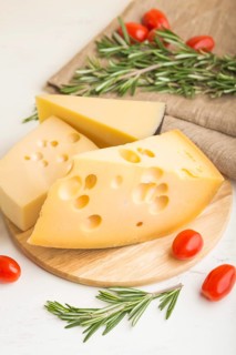 Various types of cheese with rosemary and tomatoes on wooden board on a white wooden background and