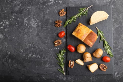 Smoked cheese and various types of cheese with rosemary and tomatoes on black slate board on a