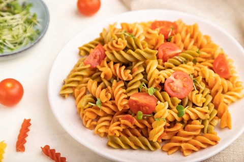 Tortiglioni semolina pasta with tomato and microgreen sprouts on a white wooden background and