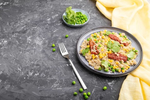 Quinoa porridge with green pea, corn and dried tomatoes on ceramic plate on a gray concrete