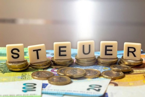 Symbolic image of taxes: The word tax is written on euro coins with letter cubes