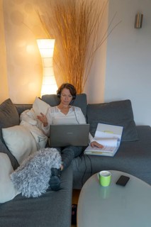 Woman, mid-50s, works from home, with laptop and communicates with colleagues via headset, home