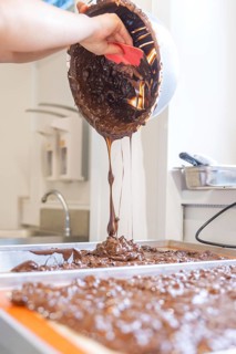 A hand pours liquid chocolate from a bowl onto a surface, Burch Schokolade production, Haselstaller