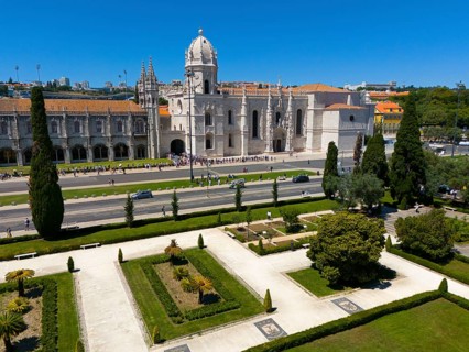 Gothic church with surrounding gardens and green areas next to a street under a clear blue sky,