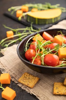 Vegetarian vegetable salad of tomatoes, pumpkin, microgreen pea sprouts on black concrete