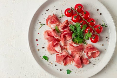 Sliced prosciutto, appetizer, with cherry tomatoes, on a white plate, top view