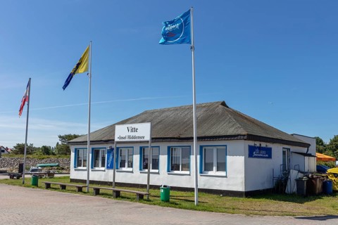 Small historic building with waving flags under a blue sky in sunny weather, Rügen, Hiddensee