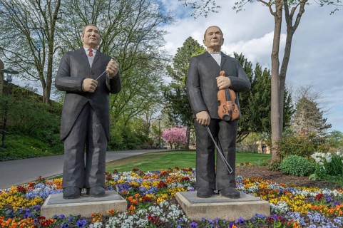 Statues of two men, one with a violin, the other with a conductor's baton, stand in a colourful