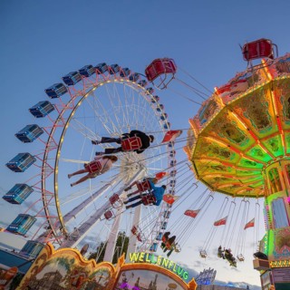 A funfair at dusk with illuminated chain carousel and Ferris wheel, Europa Rad, rides, wave flight,